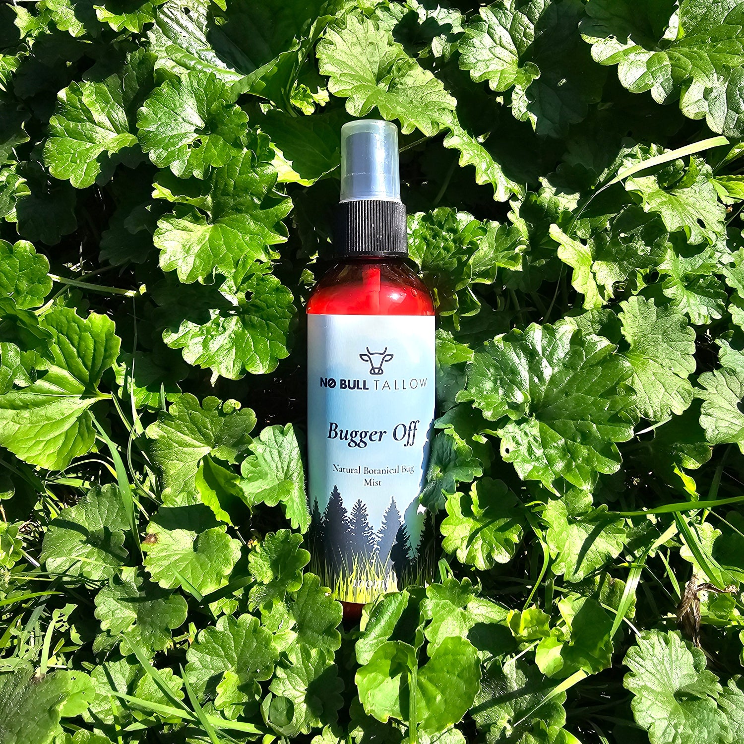A bottle of Bugger Off Bug Spray on a bed of green leafy plants in bright sunlight.