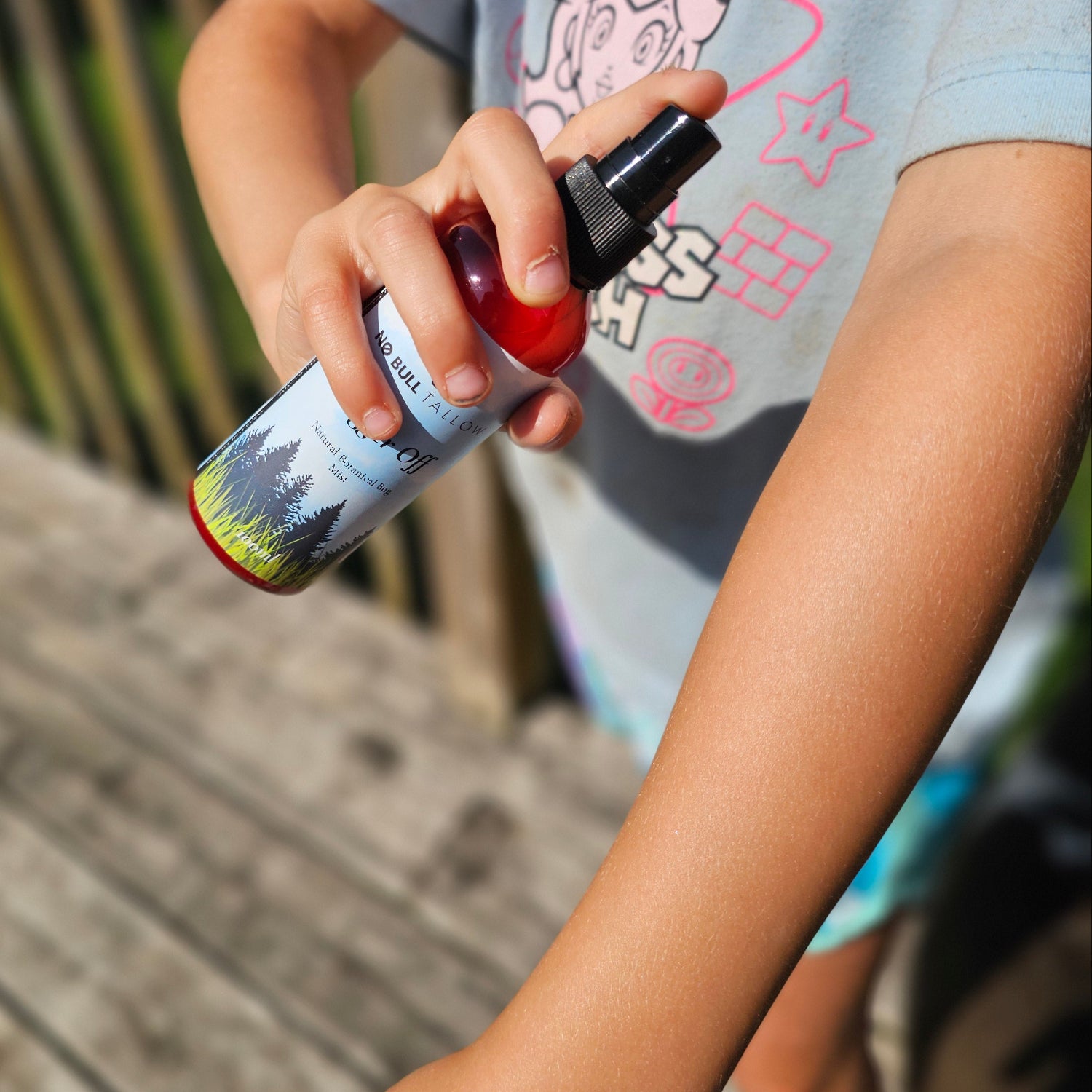 A person outdoors holds bugger off natural bug spray and uses it on arm.