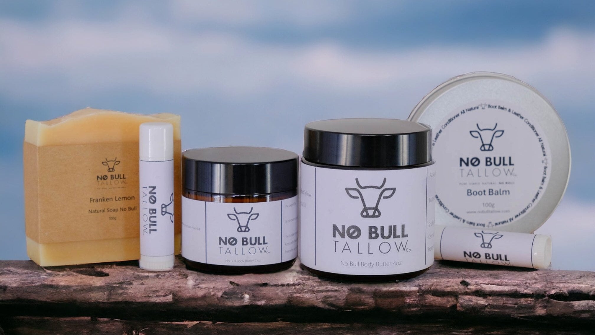 Natural no bull tallow skincare product lineup on a fence rail with a blue sky backdrop