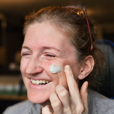 a smiling woman applying cloud cream- natural tallow moisturizer on her face